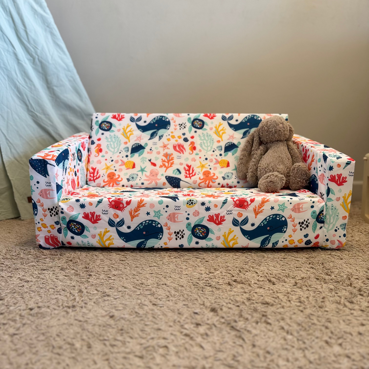 Children's sofa with animal print and a teddy bear on a carpeted floor.